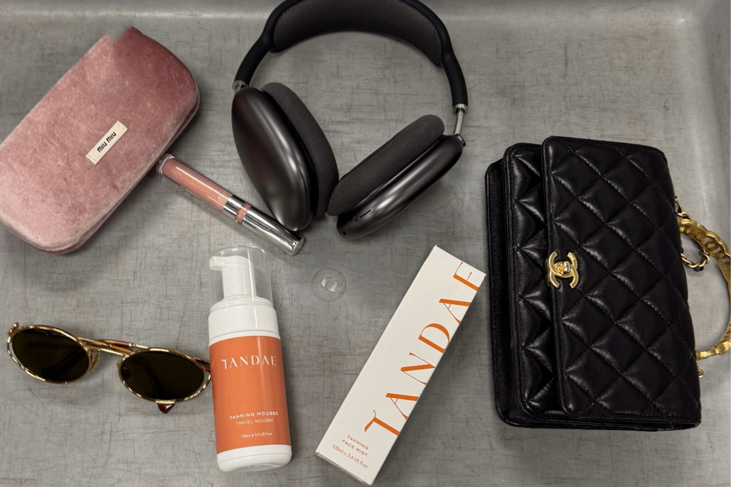 Airport security tray with sun glasses, Chanel handbag, headphones and Tandae Tanning Mousse Travel Bottle